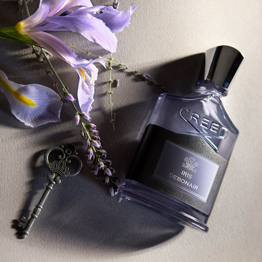 Creed Iris Debonair bottle beside pale iris flowers and an antique key